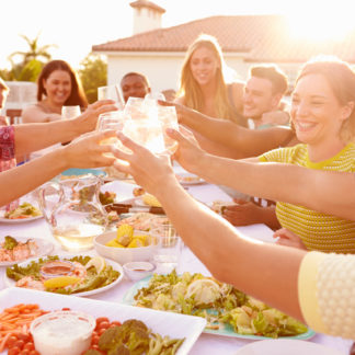 Gruppe von Freunden zu Hause draussen bei schönem Wetter am Anstossen mit Essen vom Privatkoch
