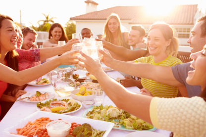 Gruppe von Freunden zu Hause draussen bei schönem Wetter am Anstossen mit Essen vom Privatkoch